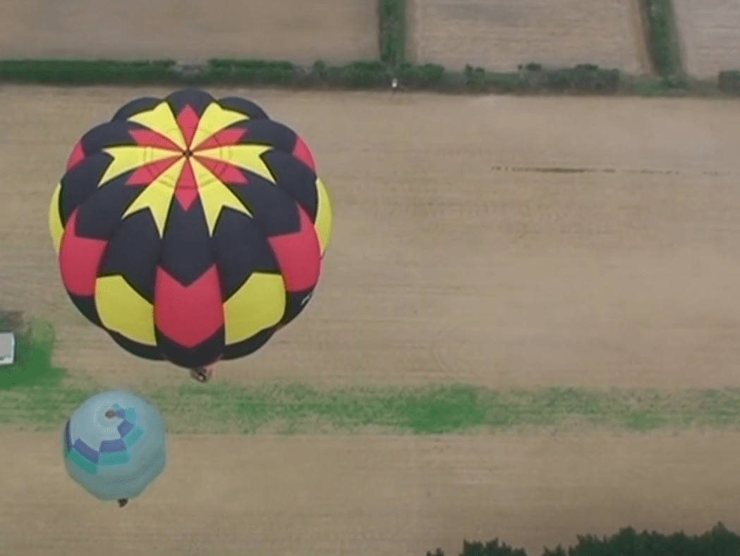 Hot air balloons rise over bare fields